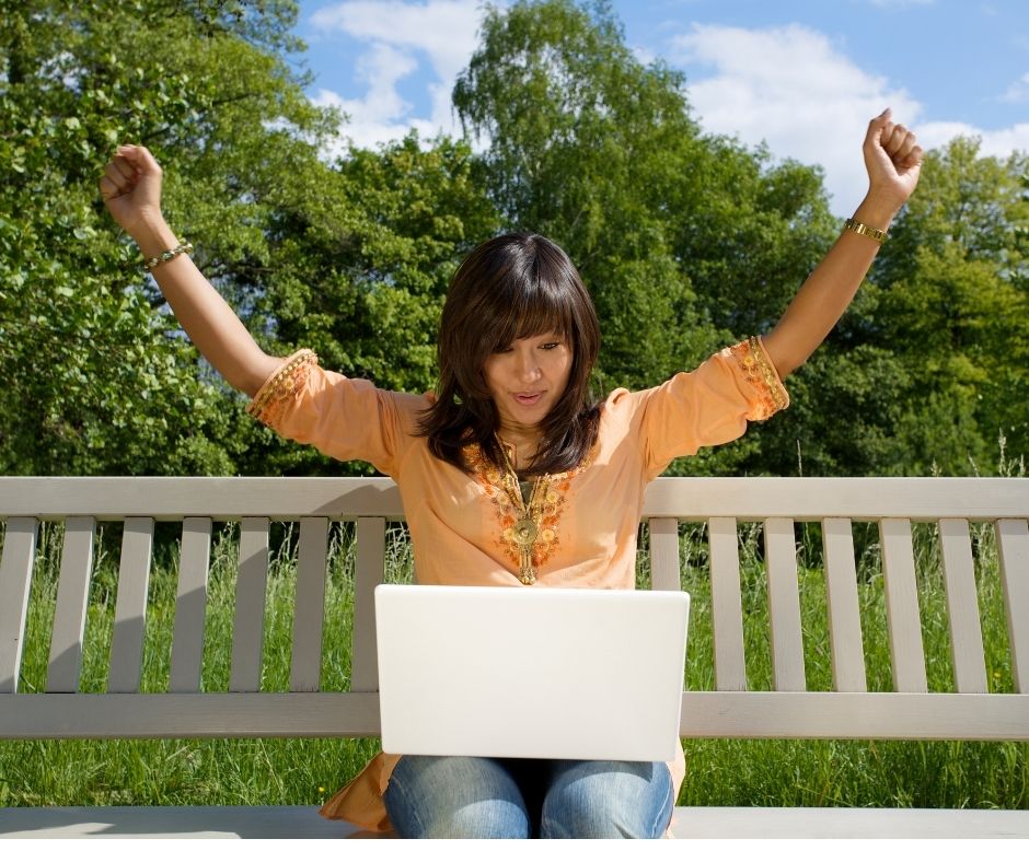 Latin woman on bench with laptop, excited about the user experience improvement